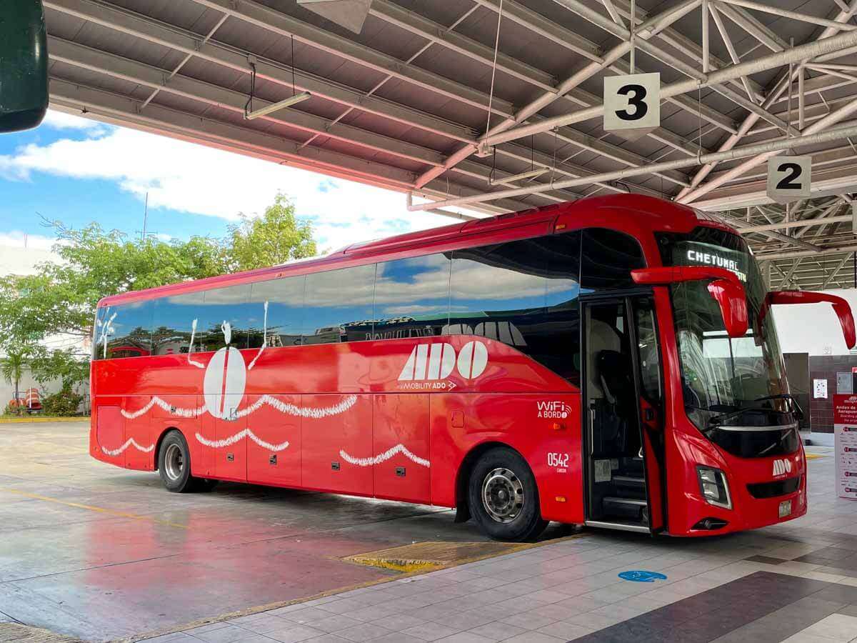 A red ADO coach parked at a numbered platform inside a bus terminal