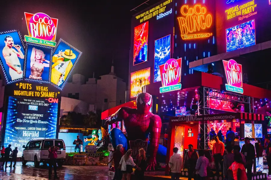 The bright neon facade of Coco Bongo at night with crowds outside