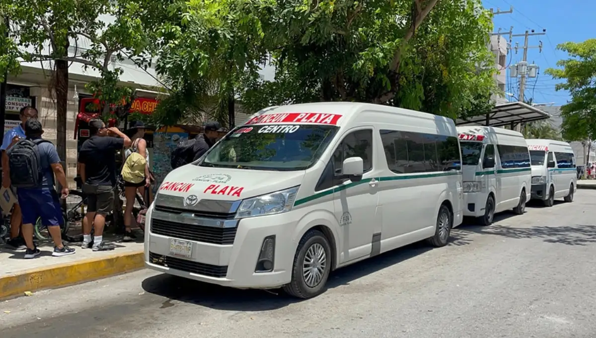 A line of white 'Cancún Playa' colectivo vans picking up passengers on a street in Playa del Carmen