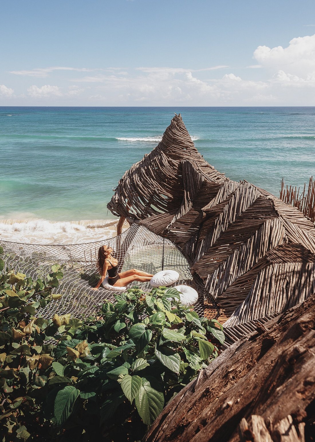 A driftwood sculpture and rope net lounge perched above the crashing sea at Azulik Tulum