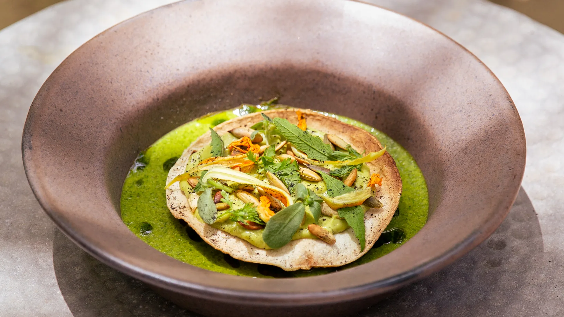A vivid green farm-to-table tostada dish plated in a rustic ceramic bowl at Our Habitas Bacalar