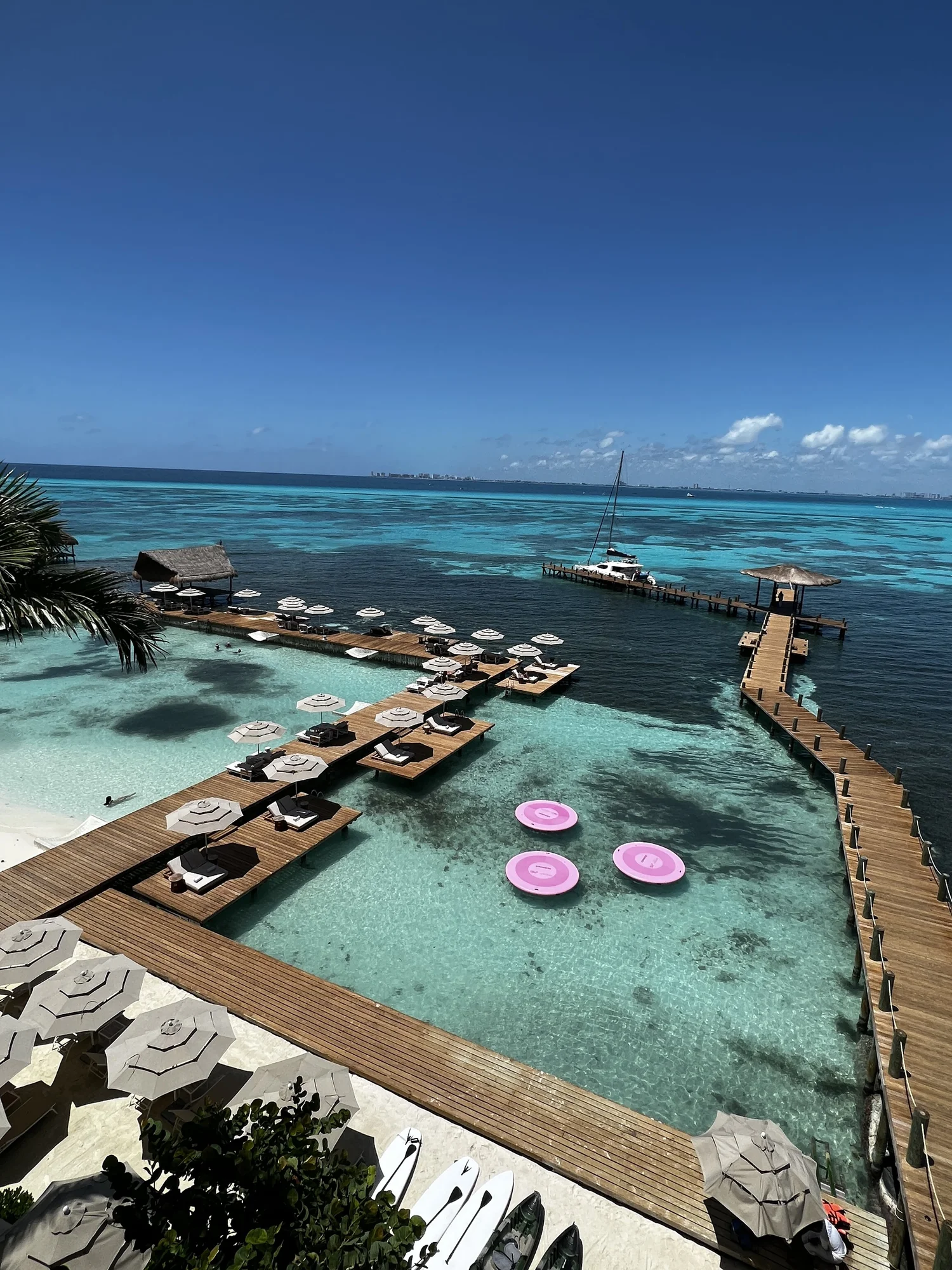 Timber sun-decks and pink floating loungers over the clear shallow bay at Impression Isla Mujeres