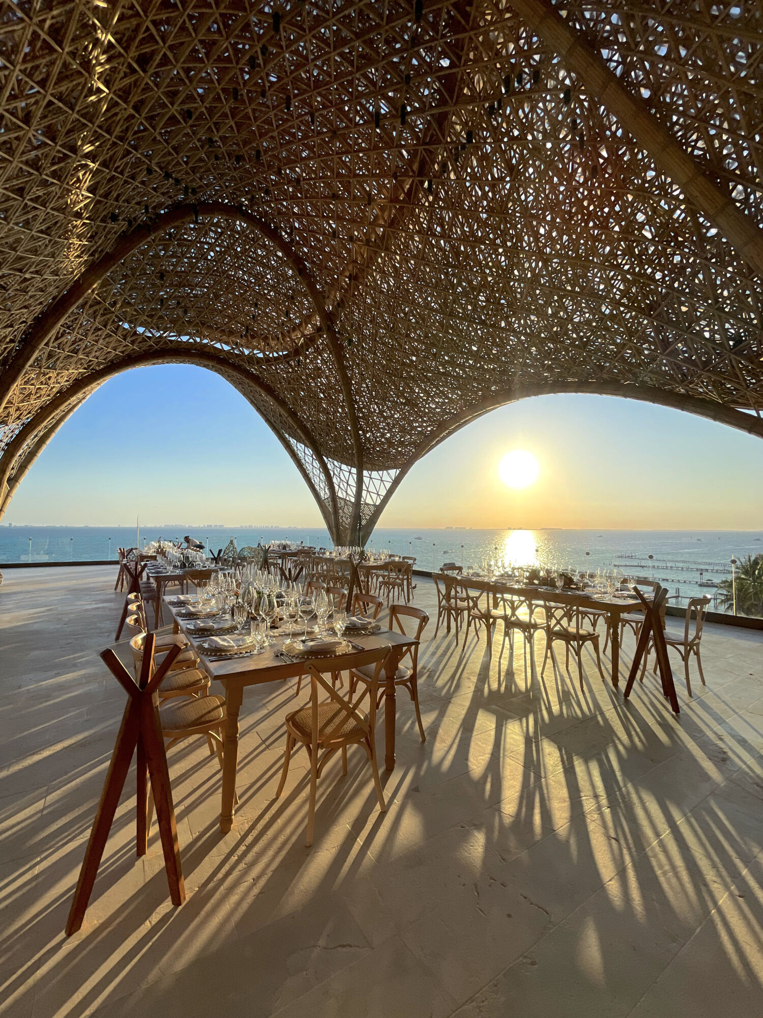 Guests dining beneath a soaring woven-bamboo canopy at sunset over the Caribbean at Impression Isla Mujeres