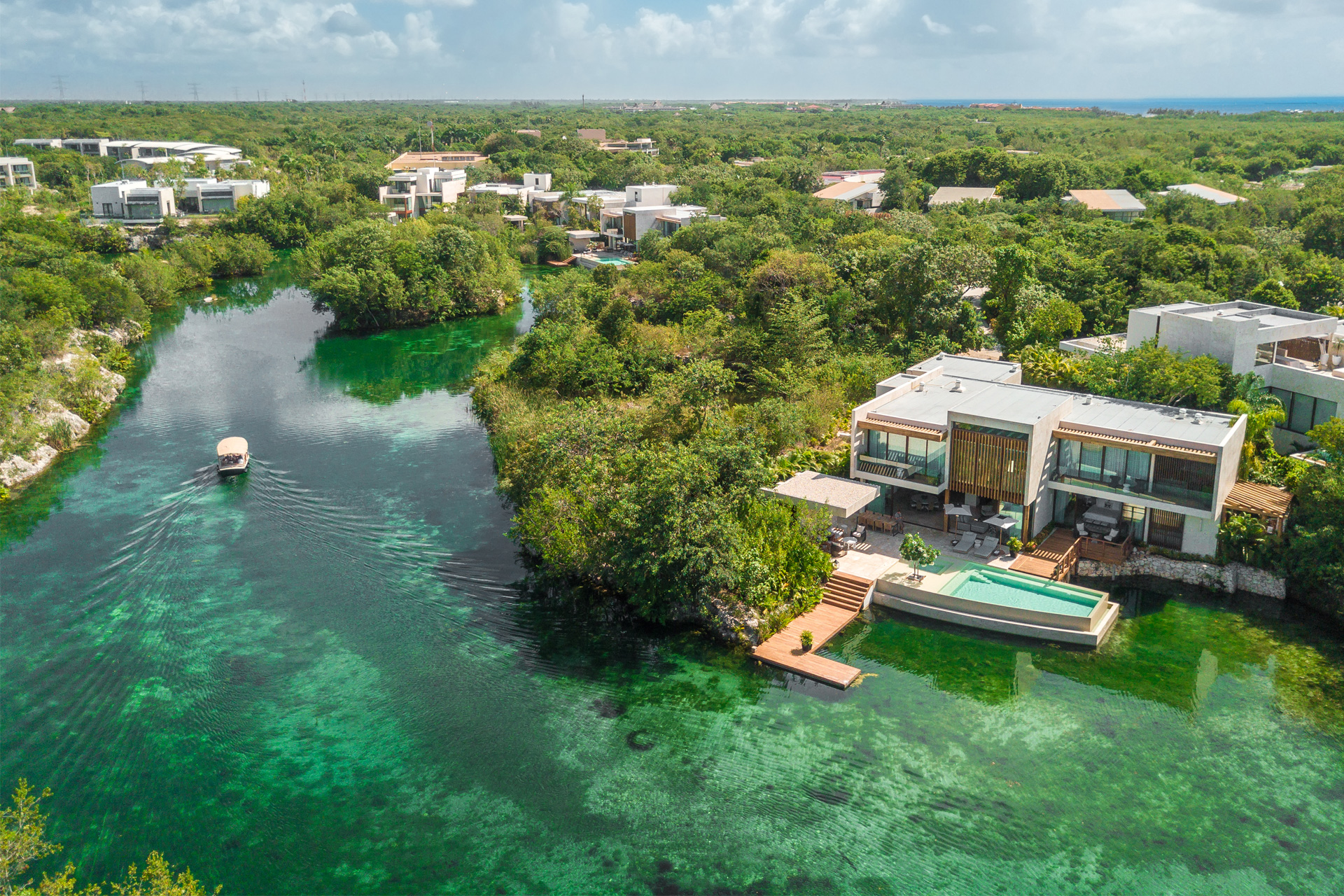 Aerial of Rosewood Mayakoba suites lining a green mangrove lagoon with a boat cruising the channel