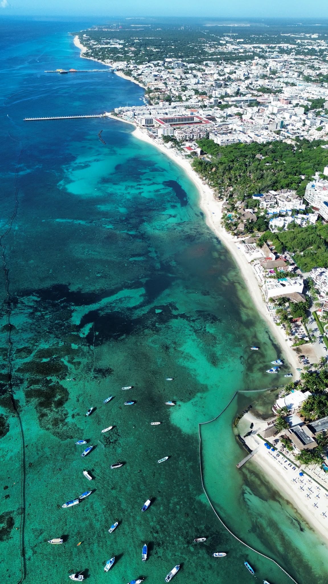 Aerial view north along the centre of Playa del Carmen on September 18, 2026, showing the ferry pier, Mamitas and the beaches around Calle 38 with clear blue and turquoise water and a containment barrier offshore